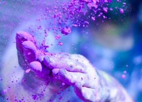 Close-up of hands throwing vibrant purple powder outdoors, capturing motion and color.